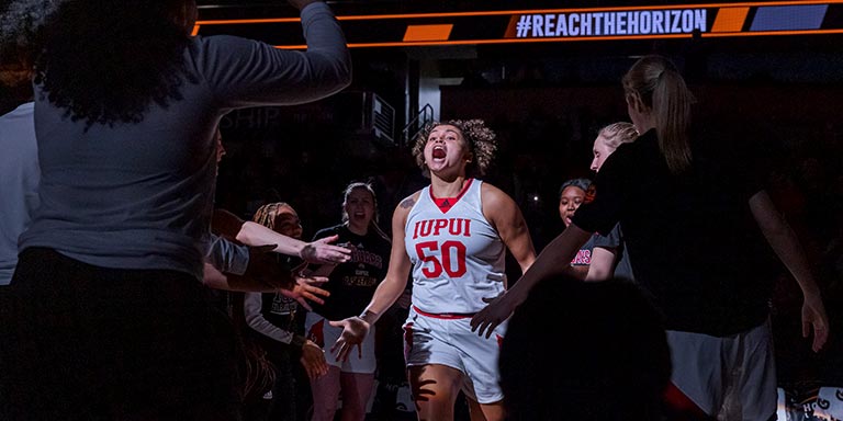 A women's basketball player yells while entering the court with her teammates around her.